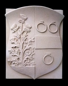 Een wapensteen met familiewapen in Bentheimer zandsteen. Het wapen bevat drie ringen, een balk en een driebloemige distel